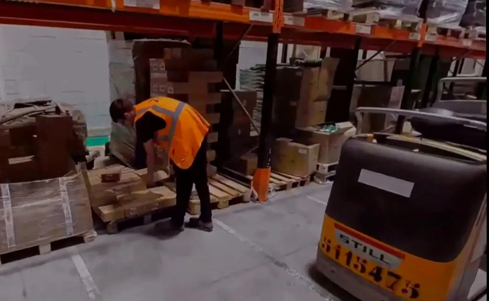 Préparateur en gilet orange penché sur une palette près d’un transpalette, chasse aux risques en réalité virtuelle