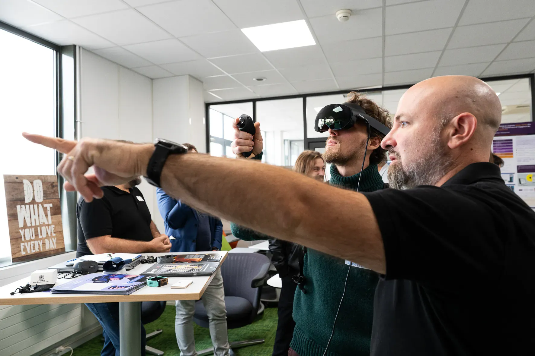 Un formateur oriente du bras un participant équipé d’un casque de réalité virtuelle.