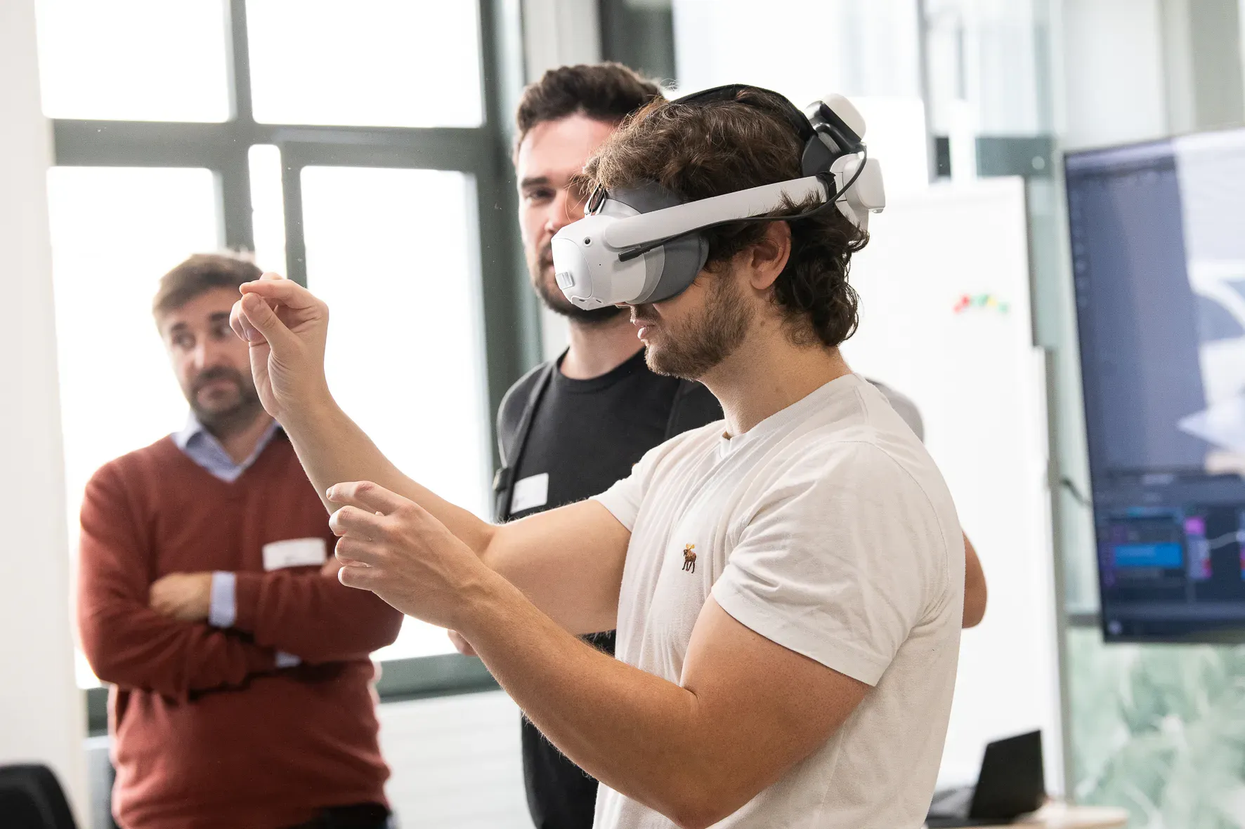 Un utilisateur en casque manipule un objet virtuel du bout des doigts, sous le regard d’un collègue.