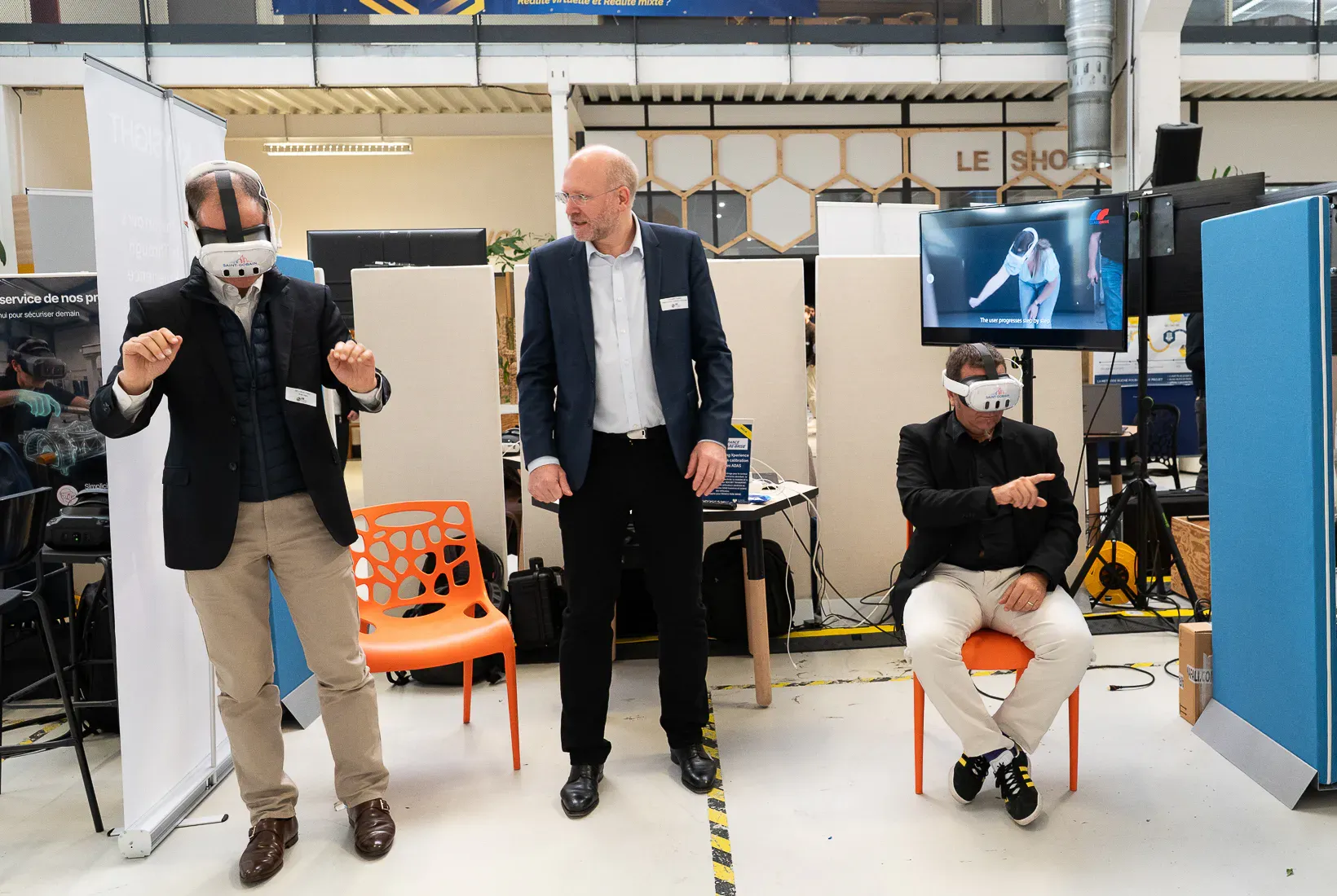 Deux visiteurs en casque de réalité virtuelle et un intervenant sur un stand de salon.