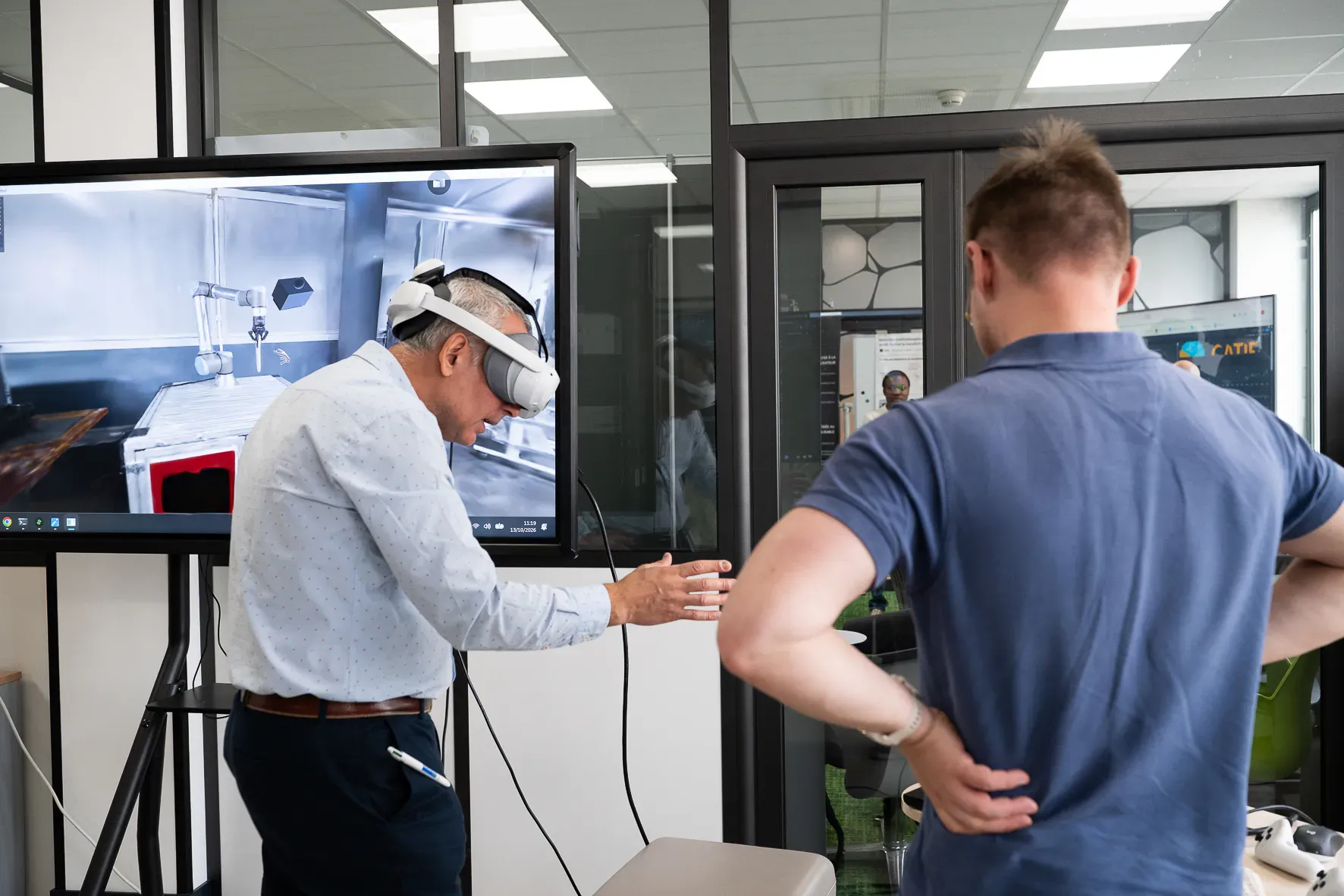 Un participant en casque manipule une scène 3D qui s’affiche en temps réel sur l’écran voisin.