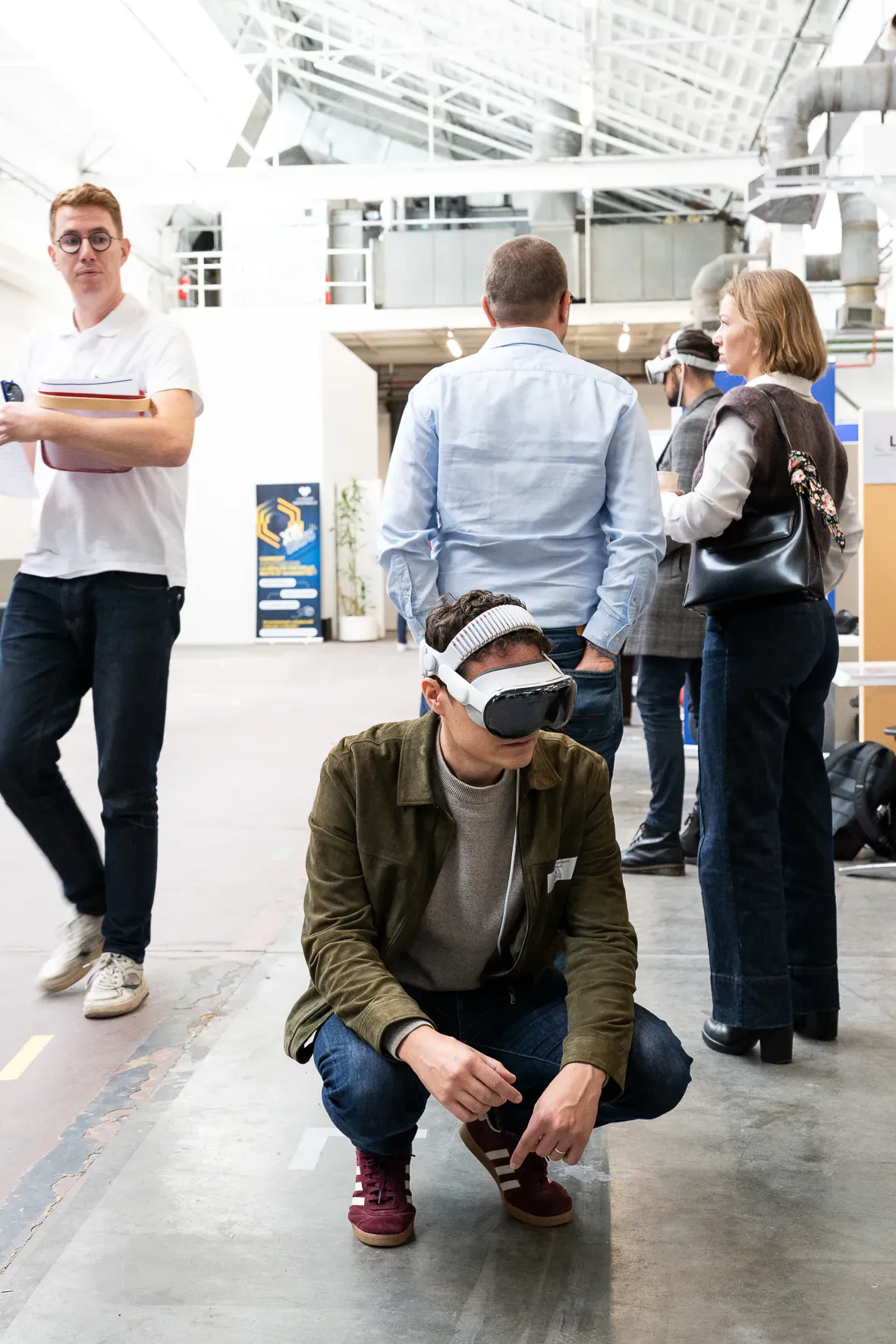 Au milieu d’un salon, un visiteur accroupi essaie un casque de réalité virtuelle.